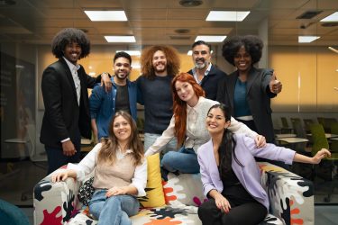 A diverse team of professionals celebrating with raised hands in a cheerful office environment.